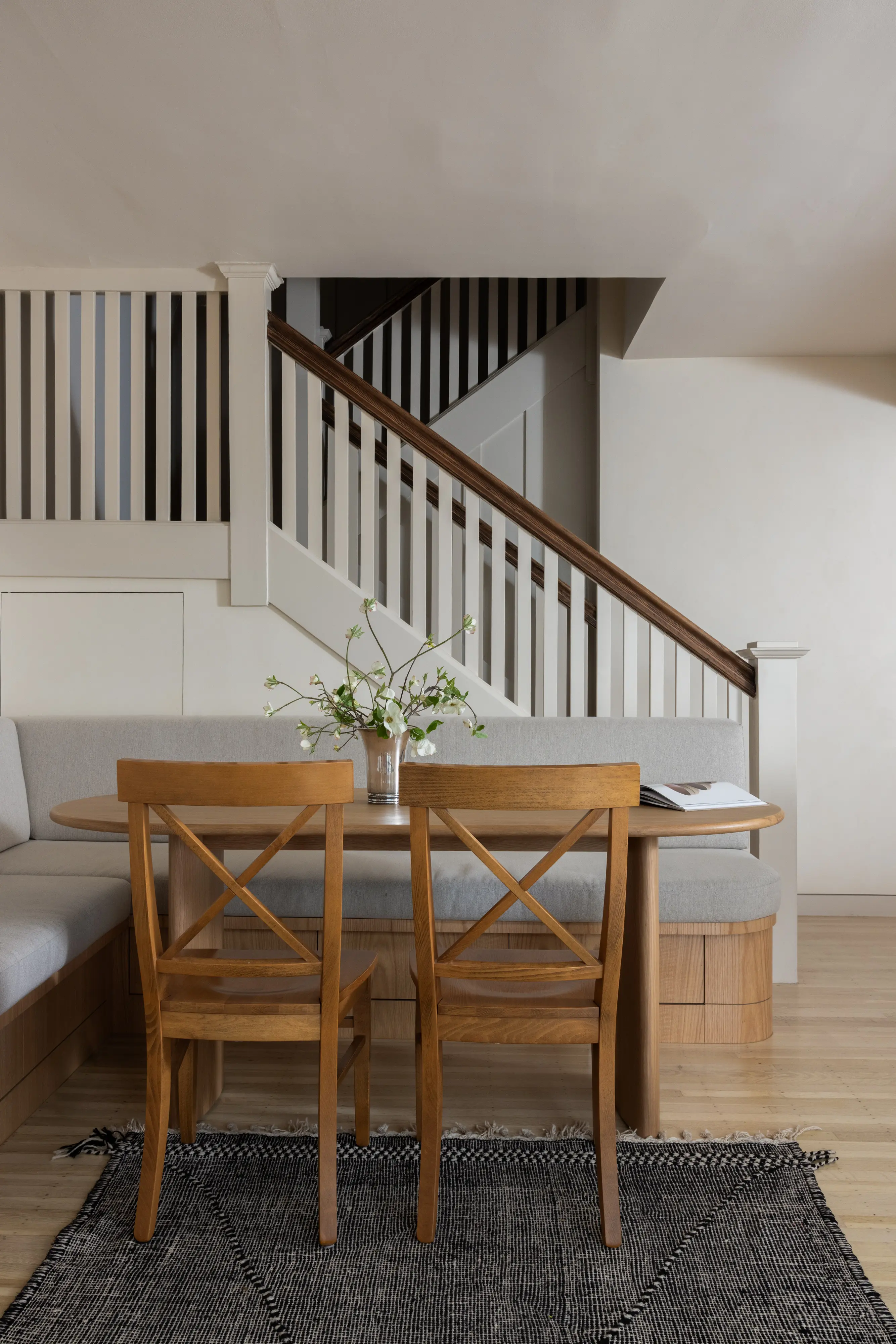 Custom red oak millwork dining banquette and oval table beside the staircase in Parnassus Heights home designed by Studio VAE, San Francisco interior designer.
